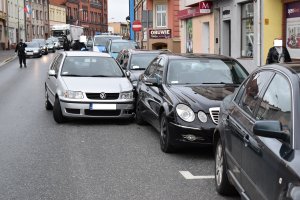 pojazdy zaparkowane na ulicy, w tle policjanci i radiowóz