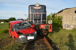 uszkodzone auto w kolorze czerwonym, stoi na szynach kolejowych z lokomotywą