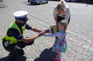 policjant klęczy przed dziećmi i wręcza odblaski w tle miasto