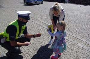 policjant klęczy przed dziećmi i wręcza odblaski w tle miasto