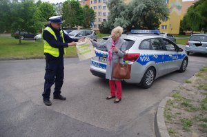 policjant wręcza rowerzystce torbę ekologiczną na zakupy,  w tle zarośla