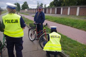 policjantki wręczają pieszym i rowerzystom elementy odblaskowe,  w tle droga i zabudowania