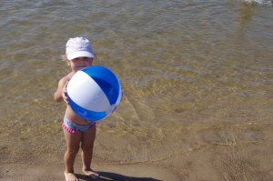 Dziecko trzyma plażową piłkę, w tle plaża