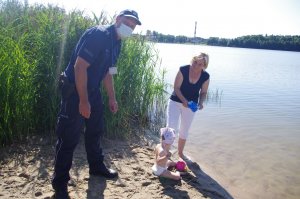 Policjanci wręczają niespodzianki dzieciom i dorosłym i ratownikom WOPR, w tle plaża