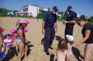Policjanci wręczają niespodzianki dzieciom i dorosłym i ratownikom WOPR, w tle plaża