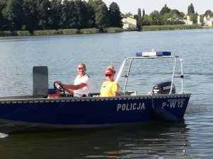 policjant i ratownik WOPR na łodzi motorowej, w tle woda
