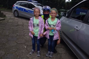 policjanci drogówki wręczają odblaski dwóm dziewczynkom, w tle radiowóz