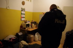 policjant umundurowany, w tle pomieszczenie- pokój z bezdomnym