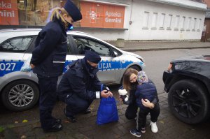 policjanci wręczają dzieciom maskotki, obok rodzice w tle zabudowania i radiowóz