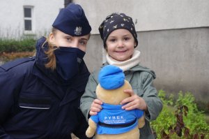 policjanci wręczają maskotki, przy dzieciach rodzice i opiekunowie w tle zabudowania