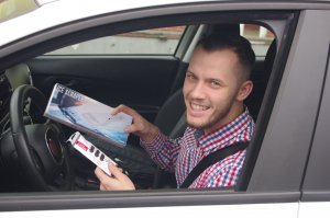 młody, uśmiechnięty mężczyzna za kierownica pojazdu pokazuje otrzymany prezent