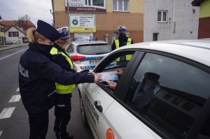 policjanci wręczają prezenty kierowcom, w tle ulica