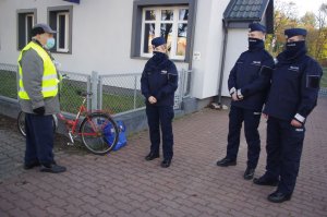 rowerzysta prezentuje na sobie otrzymaną kamizelkę, obok policjanci i posterunek policji