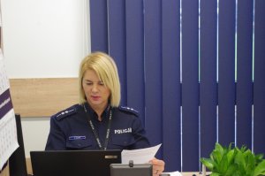 policjantka siedzi za biurkiem, w tle okno z roletami