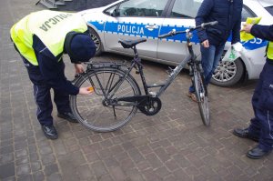 policjant zakłada odblask na koło rowerowe, w tle radiowóz