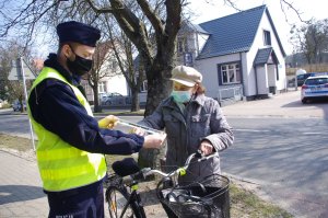 policjanci wręczają odblaski rowerzystce w tle zabudowania