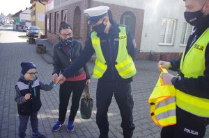 policjant wręcza odblask dziecku,  w tle ulica