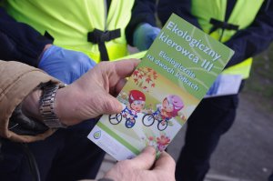 broszura trzymana w ręce przez rowerzystę, w tle policjanci