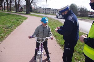 Dziewczynka na rowerze, obok policjant, w tle droga