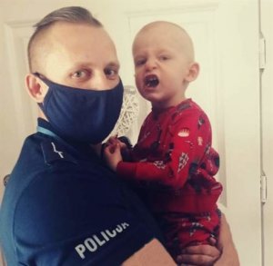 tata policjant trzyma dziecko na rękach w tle ściana pomieszczenia