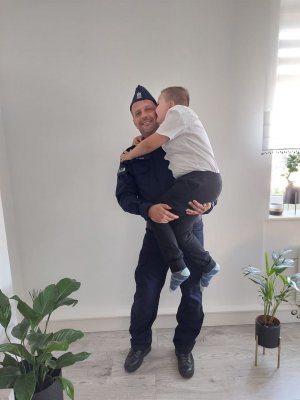 tata policjant trzyma dziecko na rękach w tle ściana pomieszczenia