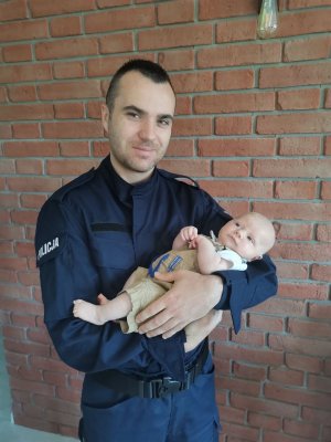 tata policjant trzyma dziecko na rękach w tle ściana pomieszczenia