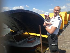tata policjant trzyma dziecko na rękach w tle jezioro i łodzie