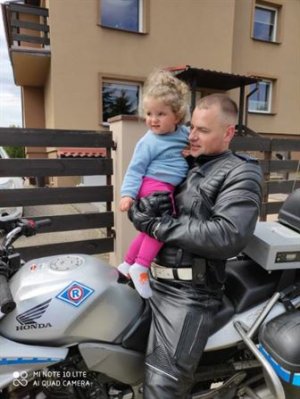 tata policjant trzyma dziecko na rękach w tle budynek