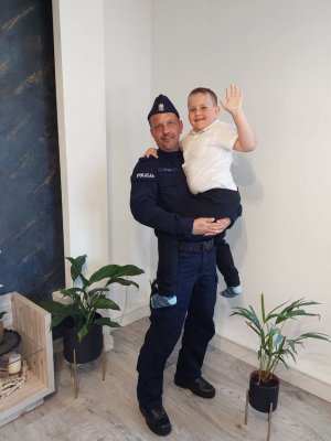 tata policjant trzyma dziecko na rękach w tle ściana pomieszczenia