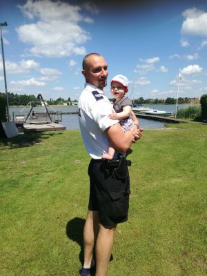 tata policjant trzyma dziecko na rękach w tle ściana zieleń
