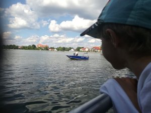 dziecko policjanta,  w tle jeziora a na nim policyjna łódź
