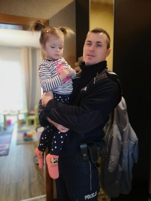 policjant trzyma na rękach dziecko, w tle mieszkanie