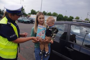 policjantka rozmawia z kobietą trzymającą na rękach dziecko w tle pojazdy