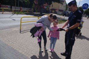 policjant wręcza  odblask dziewczynce,  w tle ulica