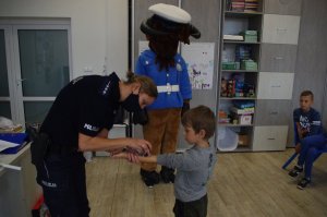 policjantka przystawia dziecku pieczątkę z wizerunkiem maskotki