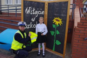 policjant z dziewczynką, w tle tablica z napisem :Witaj w szkole