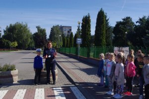policjantka uczy dzieci przechodzić przez przejście, w tle ulica