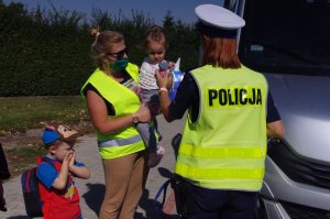 policjantka wręcza dziecku maskotkę, w tle autobus