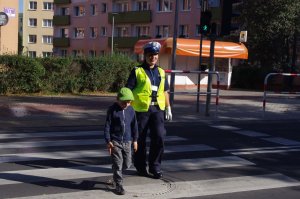 policjantka przechodzi z dziećmi przez przejście, w tle zabudowania