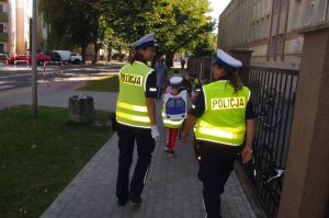 policjantki wracają z dziećmi do przedszkola w w tle zabudowania