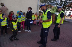 policjanci wręczają dzieciom dyplomy, w tle zabudowania