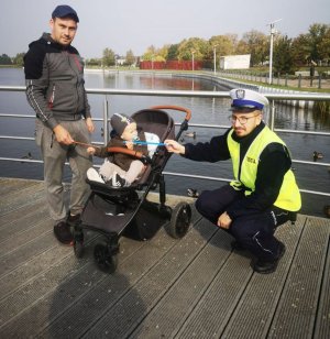 policjant wręcza odblask dziecku,  w tle jezioro