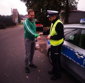 policjant wręcza odblask mężczyźnie, w tle droga