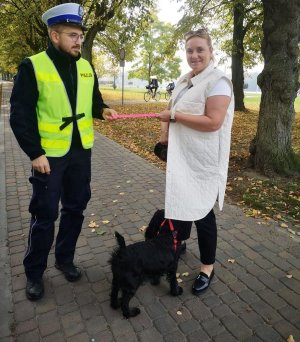 policjant wręcza odblask kobiecie, w tle droga