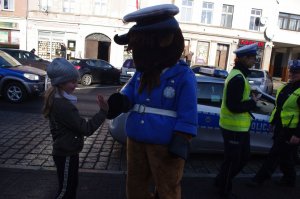 policjantka wręcza dziecku niespodziankę w tle żubrzyk i ulica