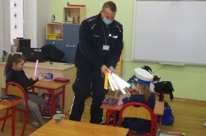 policjant wręcza dzieciom odblaski w tle klasa