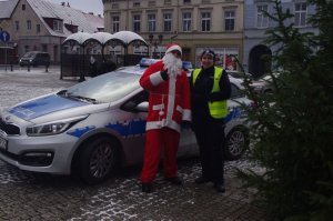 policjantka z Mikołajem przy radiowozie, w tle centrum miasta