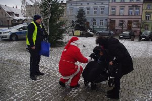Mikołaj częstuje dziecko w wózku cukierkami w tle miasto