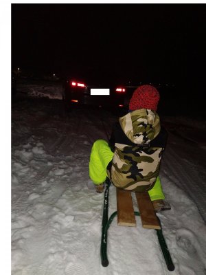 dziecko siedzące na sankach za pojazdem w tle śnieg na polu