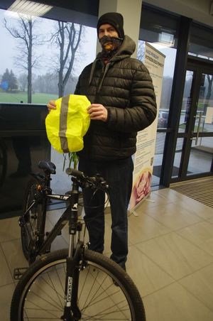 mężczyzna z rowerem trzyma odblaskowy worek na plecak,  w tle hol